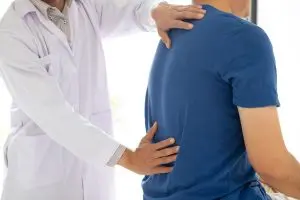 Doctor examining a male patient for back pain.
