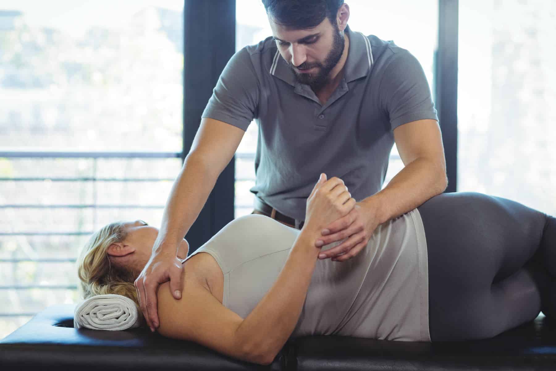 male chiropractor adjusting a female patient's shoulder