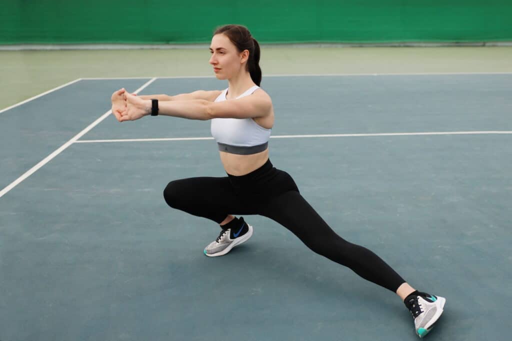 Female athlete stretching on outdoor tennis court, wearing sportswear