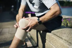 Adult man sitting on a side walk holding his knee due to pain. Stem cell therapy treatment can help relieve the pain.