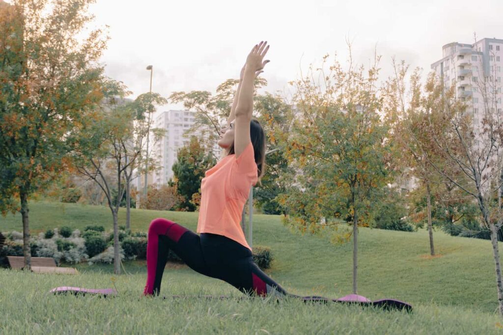 Woman in activewear performing yoga lunge pose in a vibrant green city park