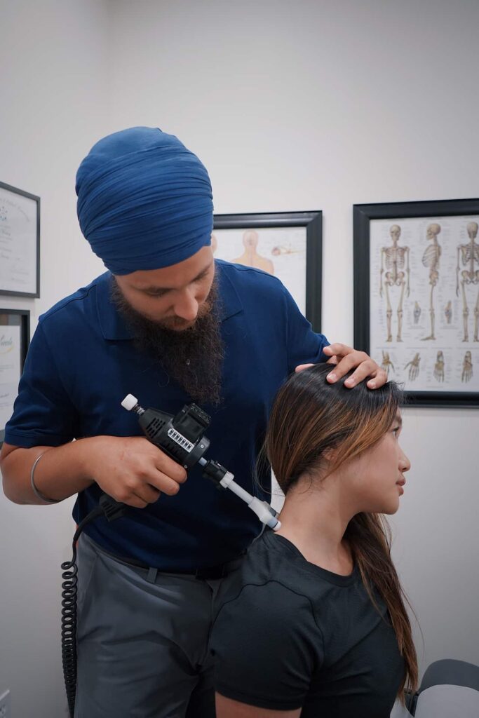 Chiropractor performing neck adjustment on woman in a clinical setting with anatomical charts.