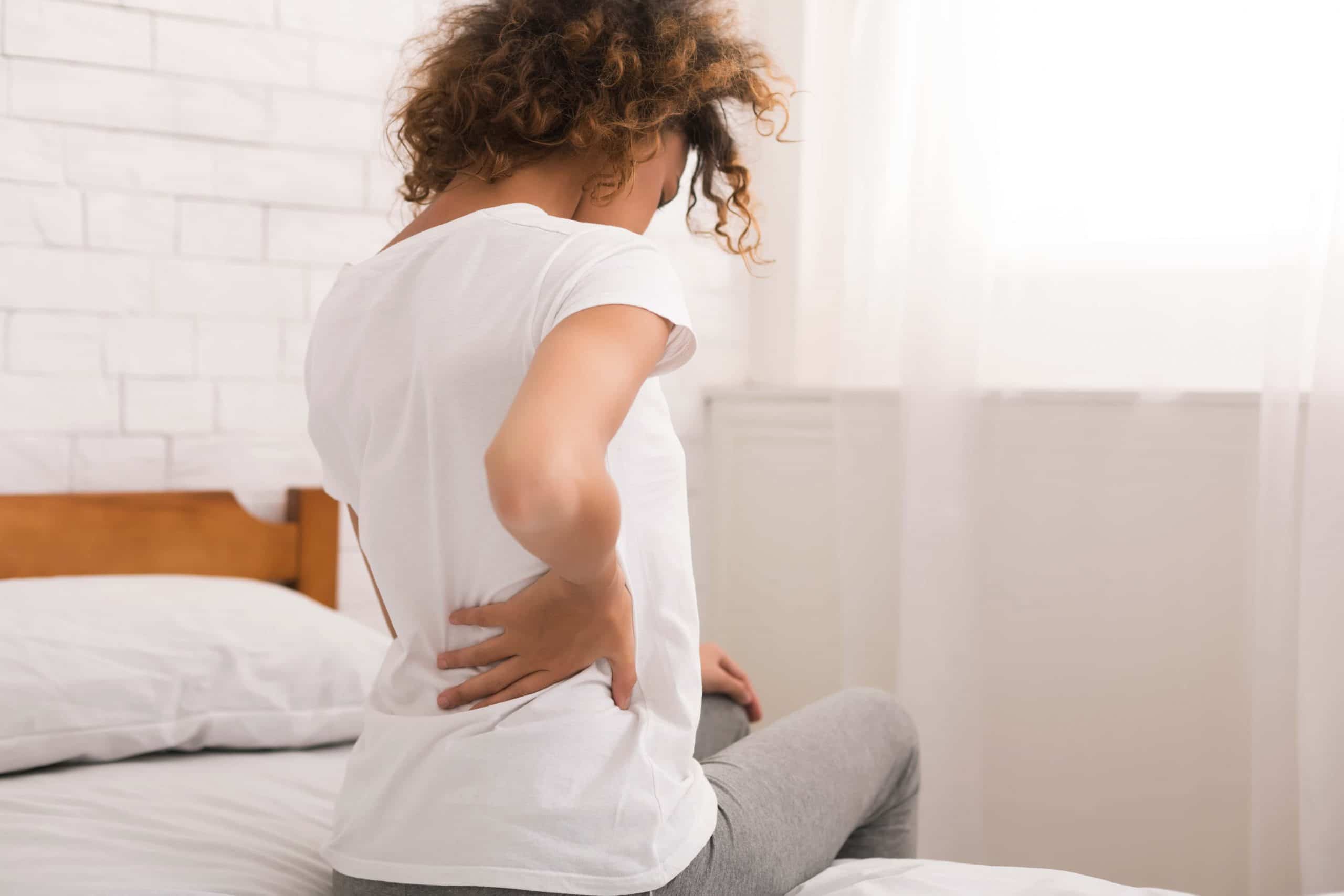woman sitting on her bed experiencing Spondylolisthesis pain
