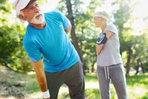 A senior man with back pains and a woman standing on grass