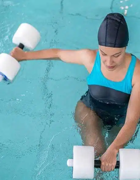 The woman having physical therapy in a pool with styro dumbells