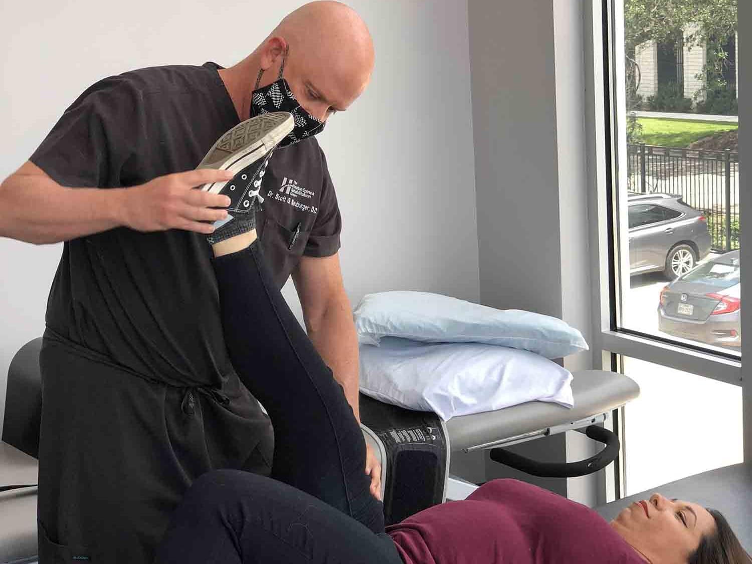 Woodlands chiropractor, Dr. Neuburger, doing adjustments to a patient's leg on a chiropractic table