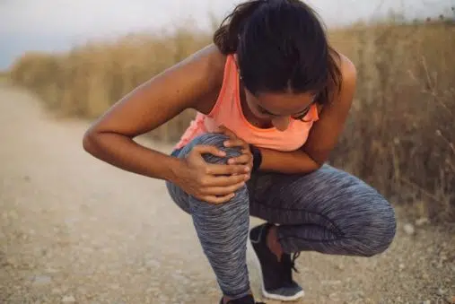 Female athlete suffering form running knee or kneecap injury during outdoor workout on dirt road.