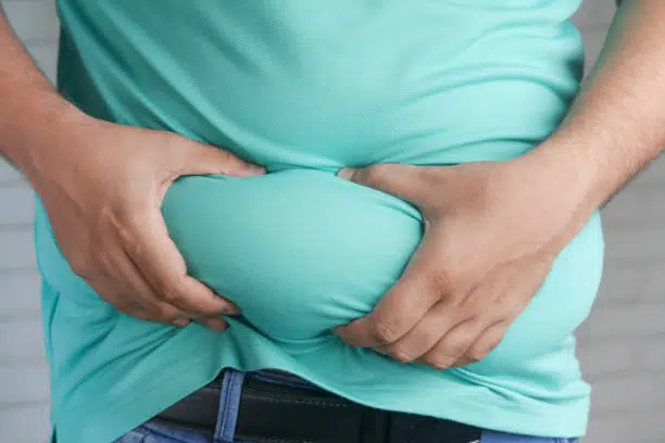 man's hand holding excessive belly fat, overweight concept.