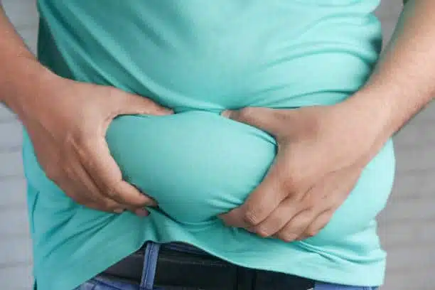 man's hand holding excessive belly fat, overweight concept.