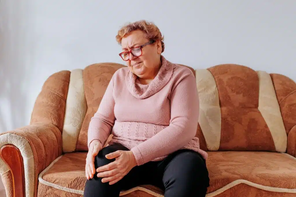 Woman suffering from intense leg pain while sitting on a couch at home.