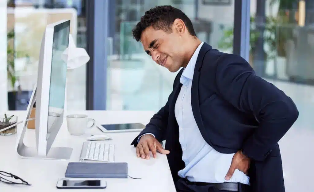 Man suffering from intense back pain while sitting in his office chair at work.