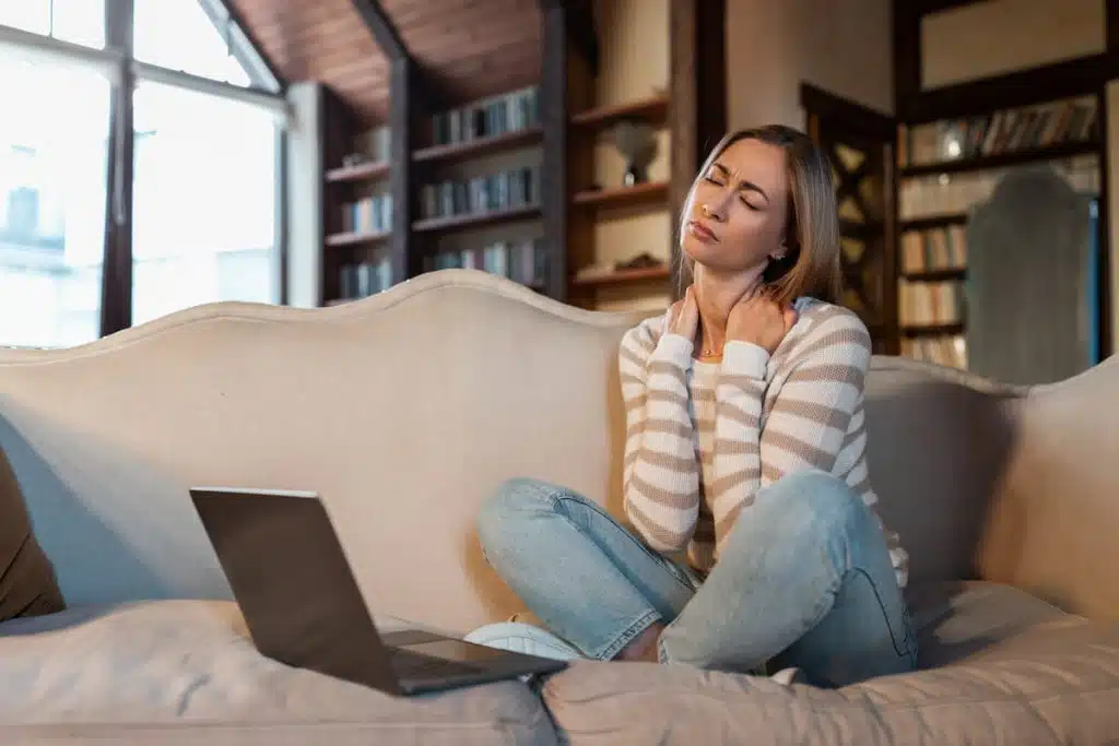 young woman experiencing back and neck pain while working on the couch.