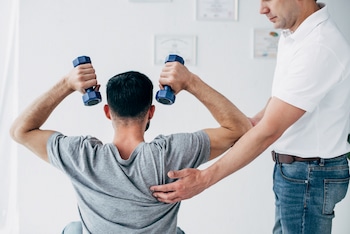 A chiropractor massaging shoulder of man with dumbbells in hospital