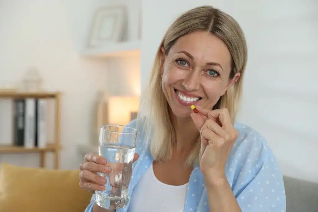 A woman swallowing a pellet pill while smiling