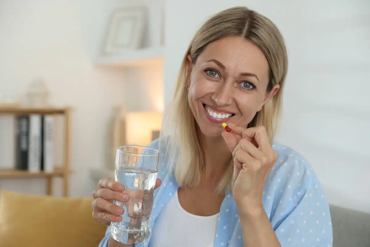 A woman swallowing a pellet pill while smiling