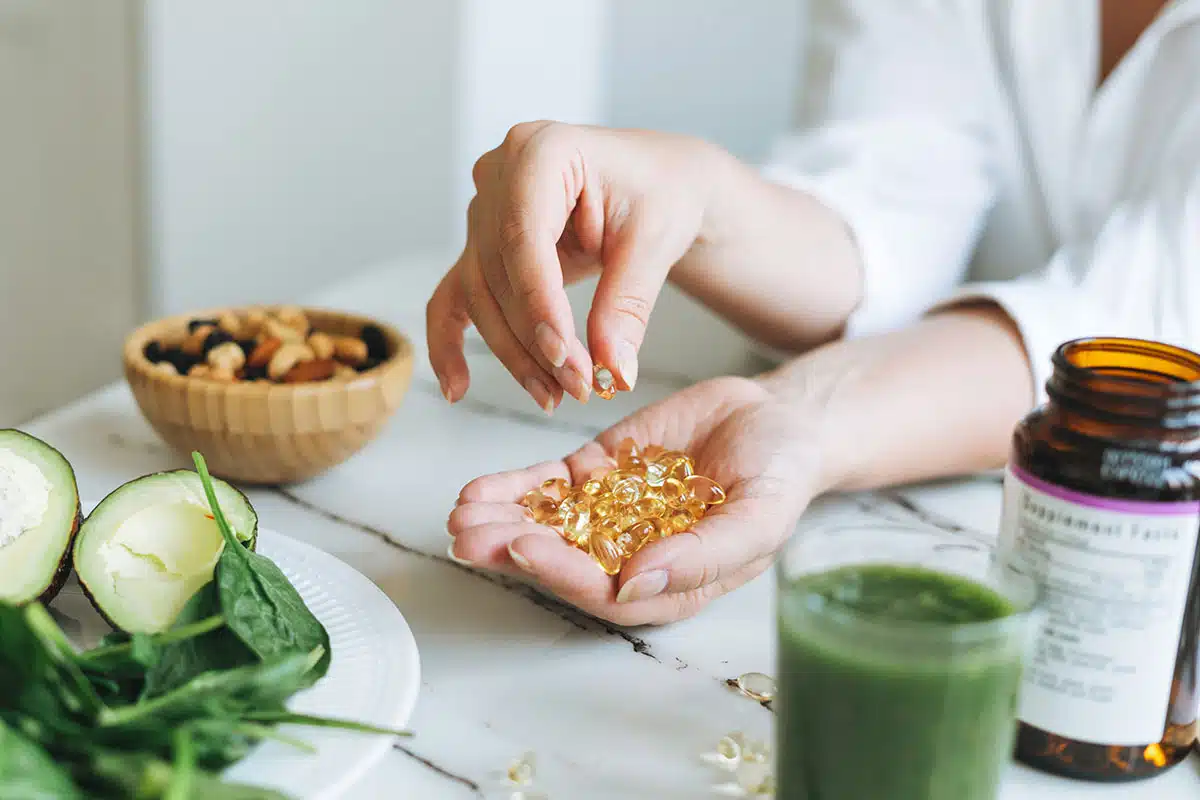 Woman doctor nutritionist hands in white shirt with omega 3, vitamin D capsules with green vegan food. The doctor prescribes a prescription for medicines and vitamins at the clinic